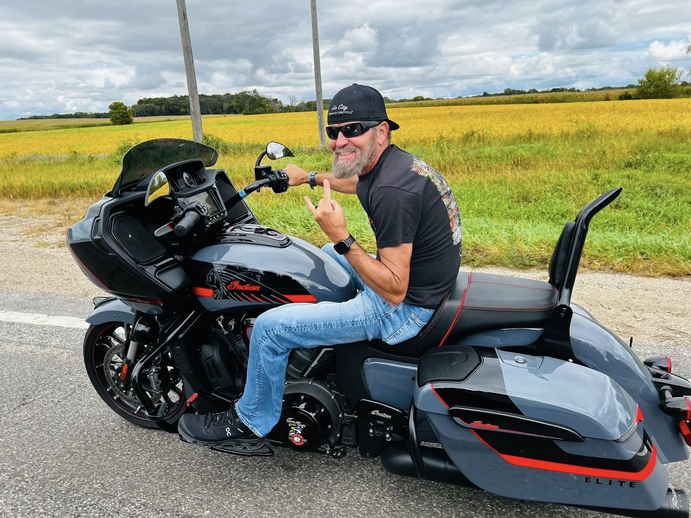 A smiling rider on a grey Indian bagger beside a field